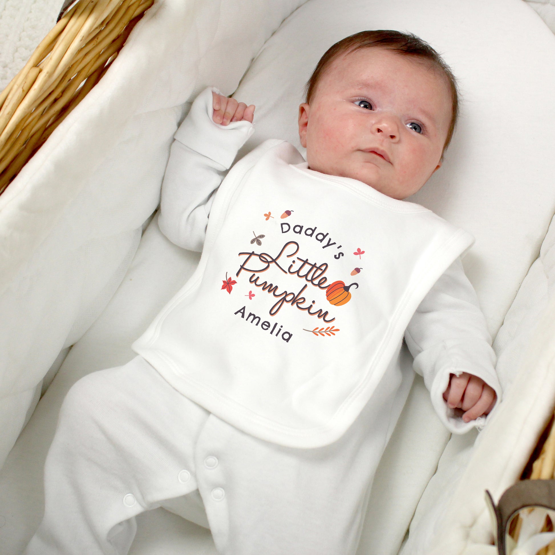 Newborn baby wearing a bib with 'Daddy's Little Pumpkin Amelia' text, lying on a white blanket.
