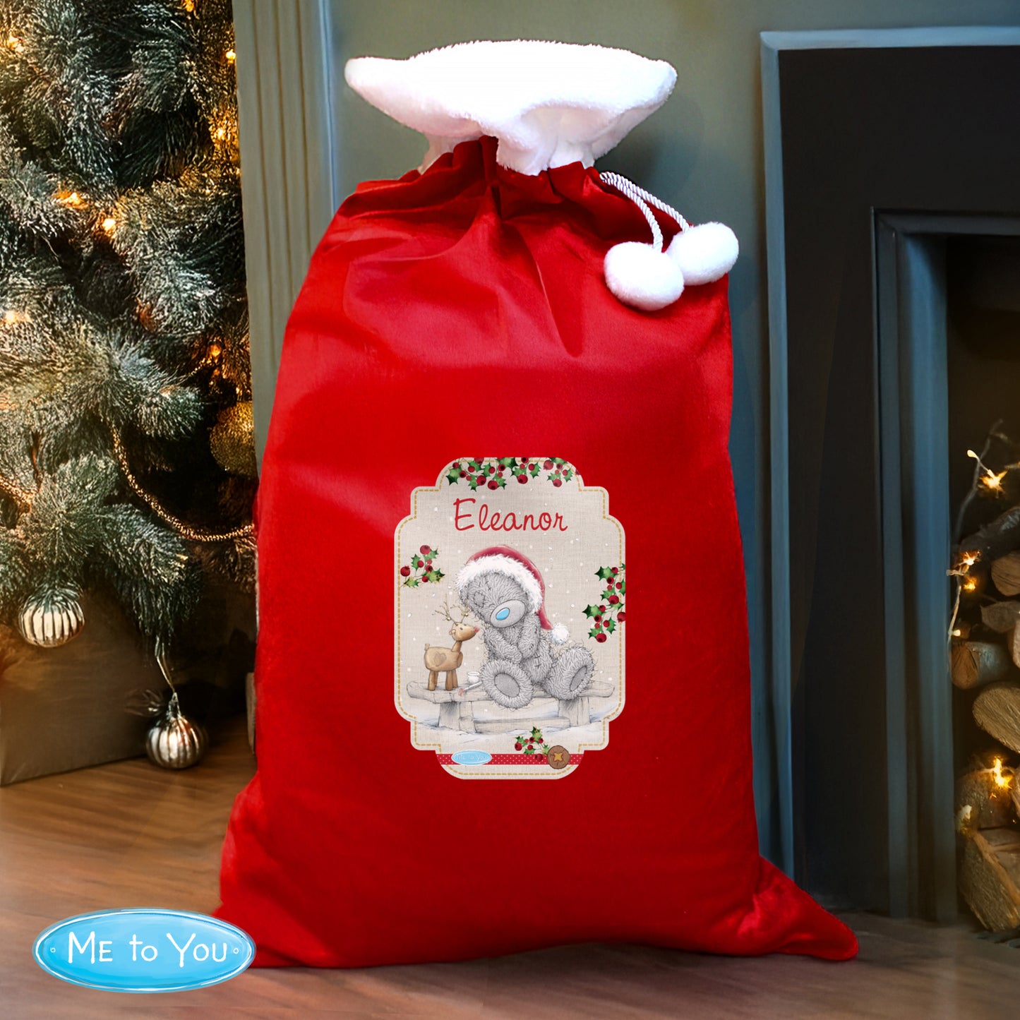 Red Christmas sack with a personalised label featuring a teddy bear design, placed in front of a decorated Christmas tree.