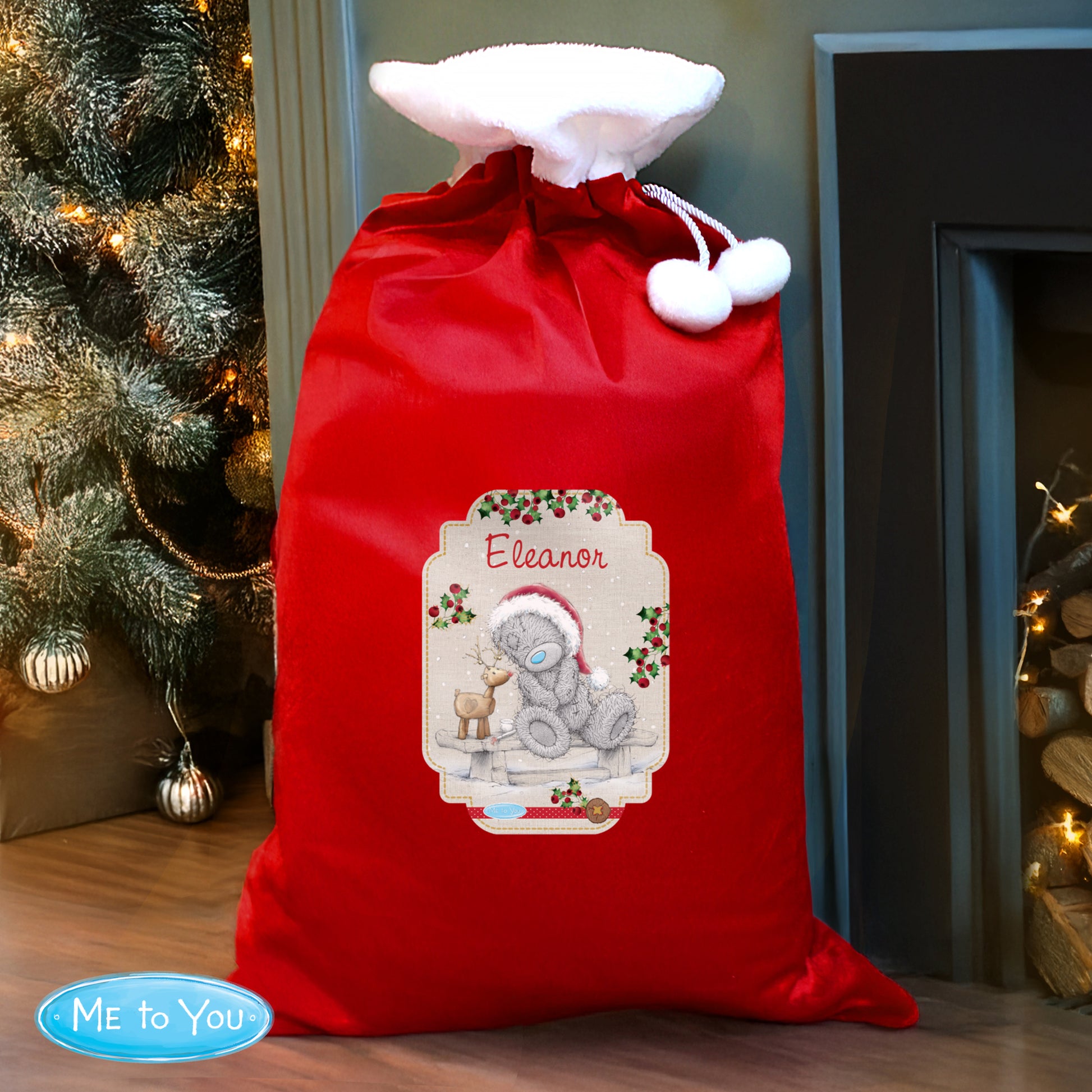 Red Christmas sack with a personalised label featuring a teddy bear design, placed in front of a decorated Christmas tree.