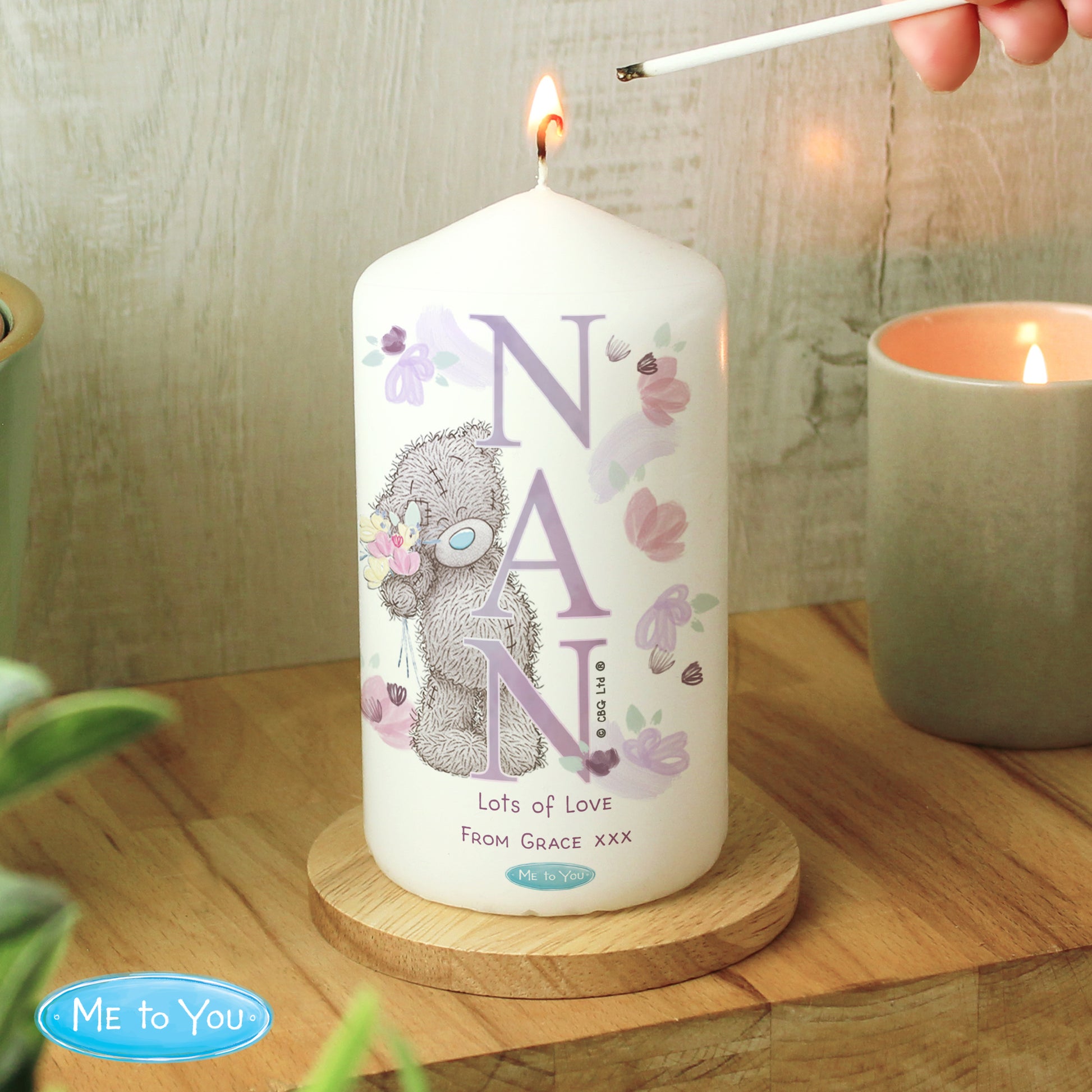 Candle with 'NAN' and a teddy bear design, being lit on a wooden surface.
