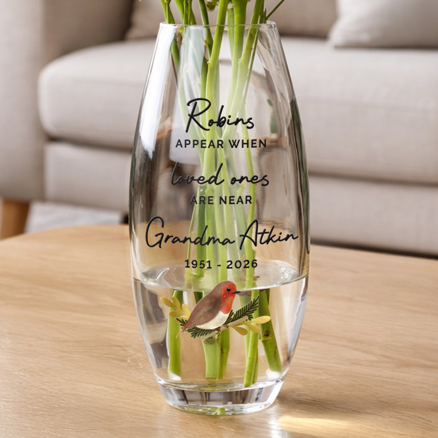 Clear glass vase with engraved text and a bird illustration on a wooden table.