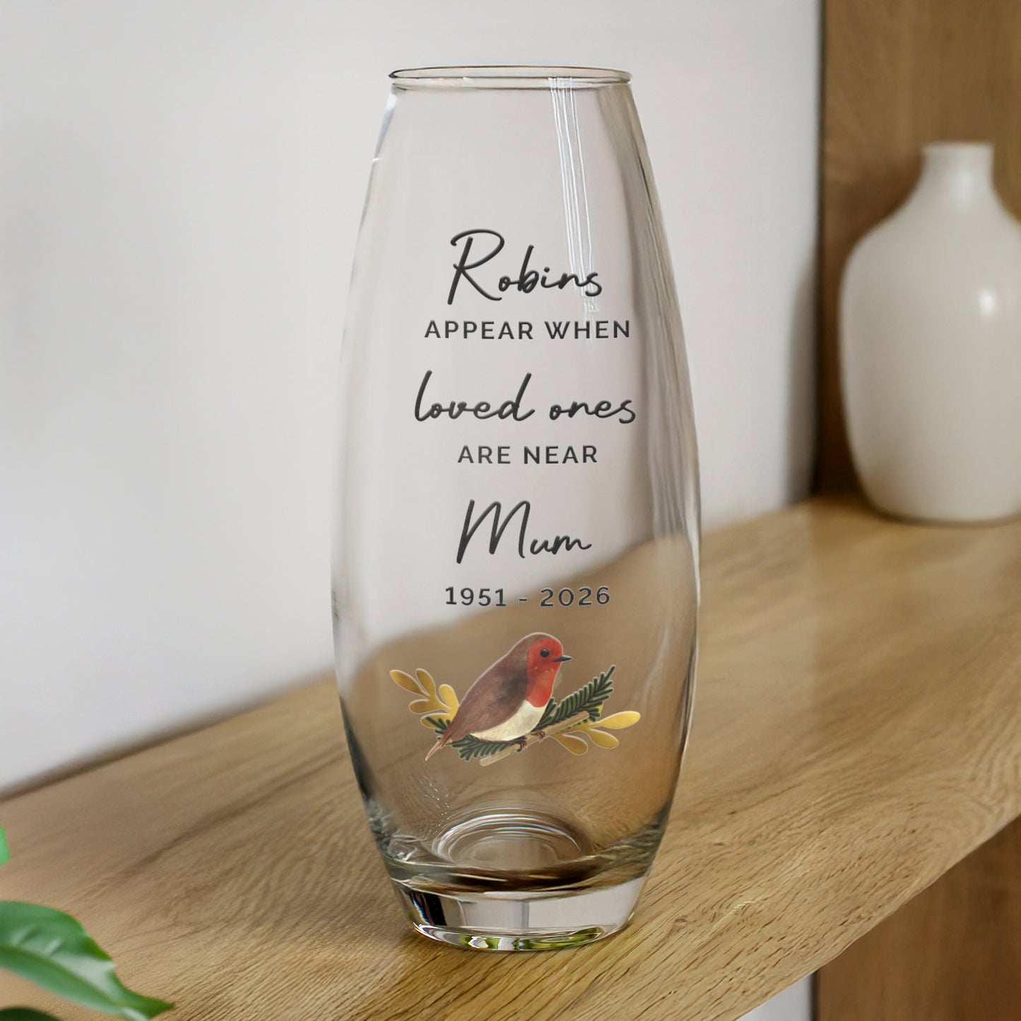 Clear glass vase with engraved text and robin design on a wooden surface.