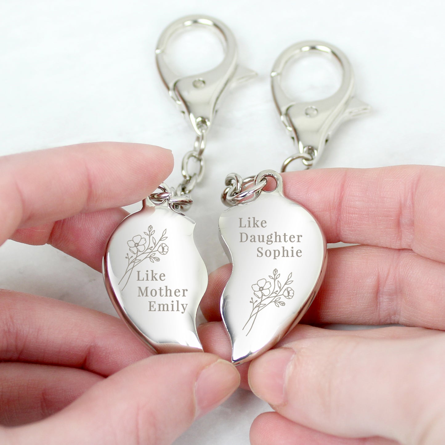 Personalised Mother daughter Keyring showing the heart in two pieces. Each piece fits to make the complete heart. Each is a separate keyring. One has the message Like Mother Emily and the other shows Like Daughter Sophie. Each piece has an engraved floral spray.Made from Nickel.