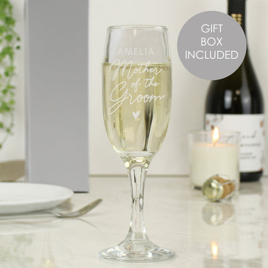 Personalised champagne flute with champagne, gift box, and candle on a table.