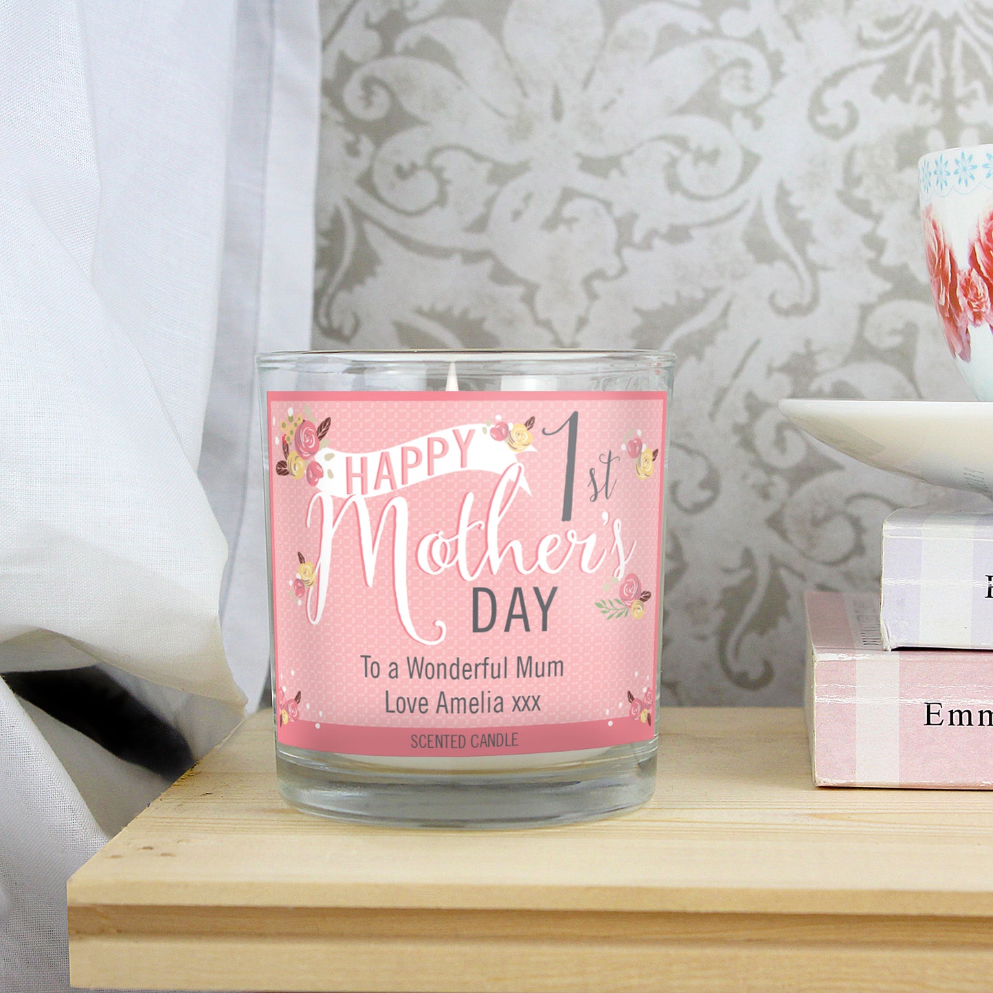 Personalised 1st Mother's Day Scented Candle shown alight standing on a bedside cabinet.