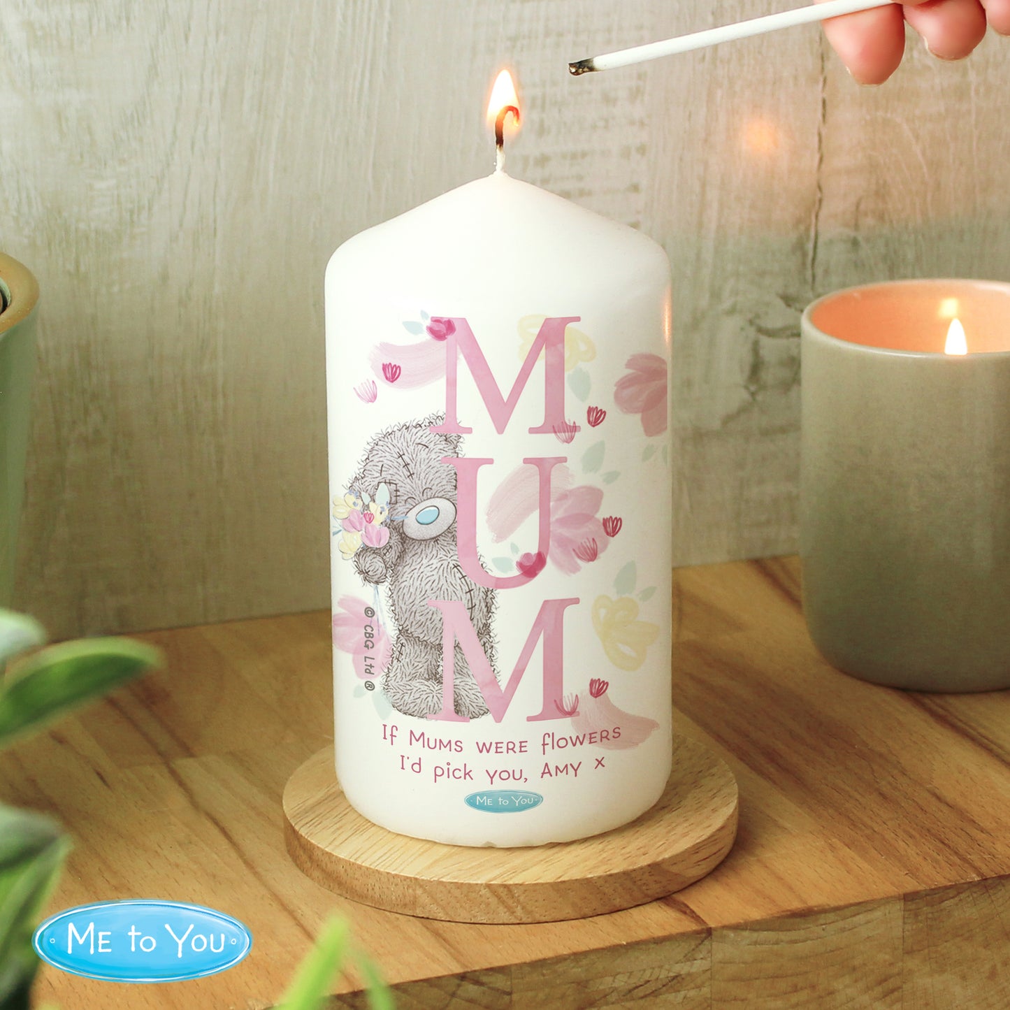Candle with 'MUM' text and a bear illustration, being lit on a wooden surface.