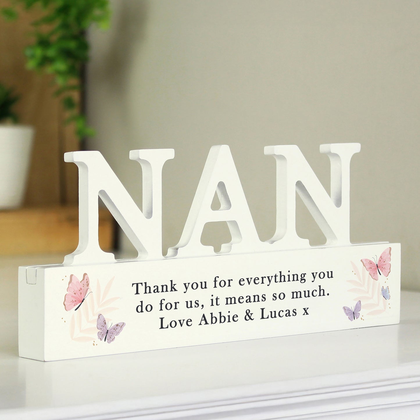 White decorative sign with 'NAN' and a message on a white surface.