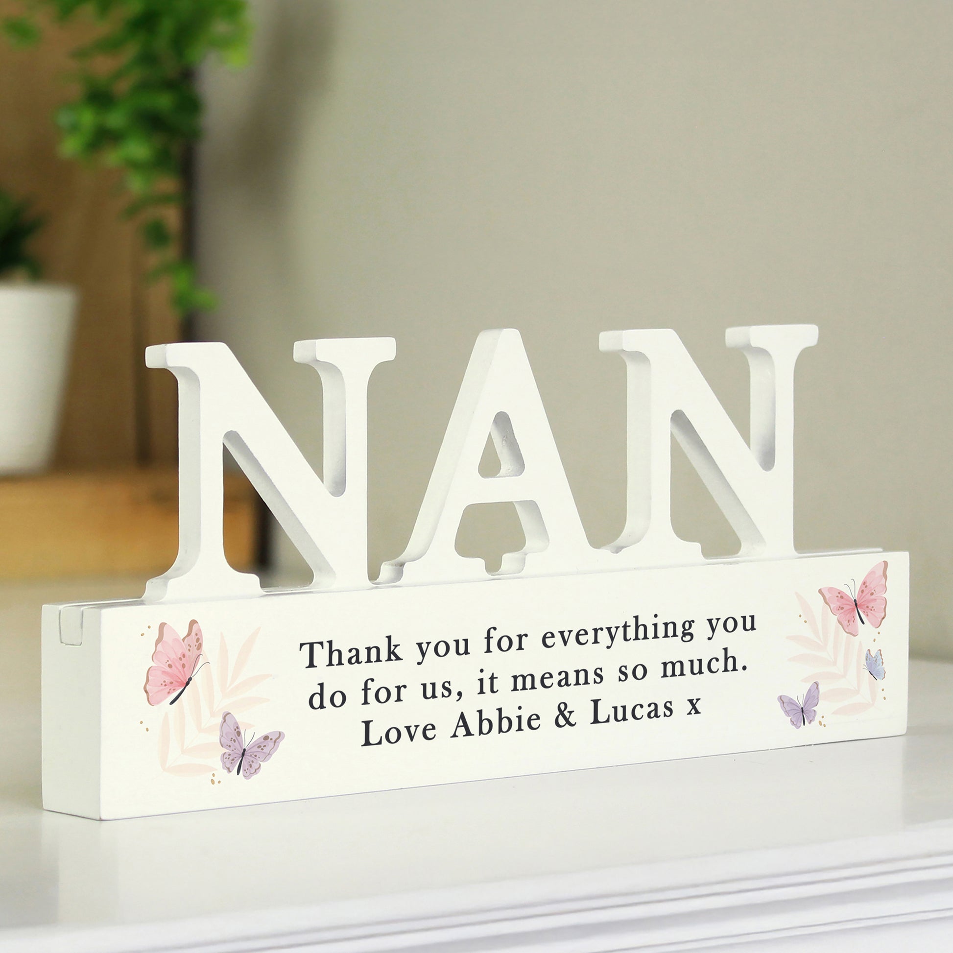 White decorative sign with 'NAN' and a message on a white surface.