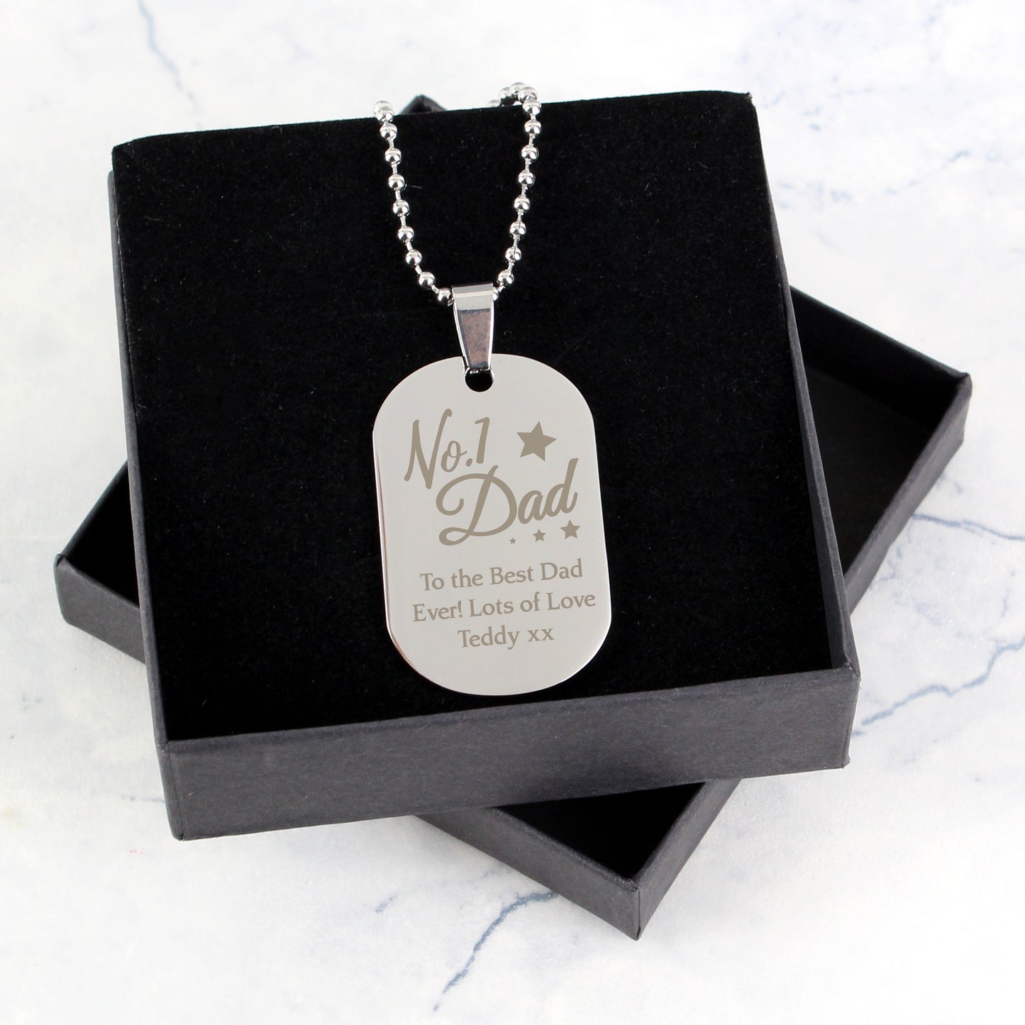 Silver dog tag necklace with engraved message in a black box on a light grey background