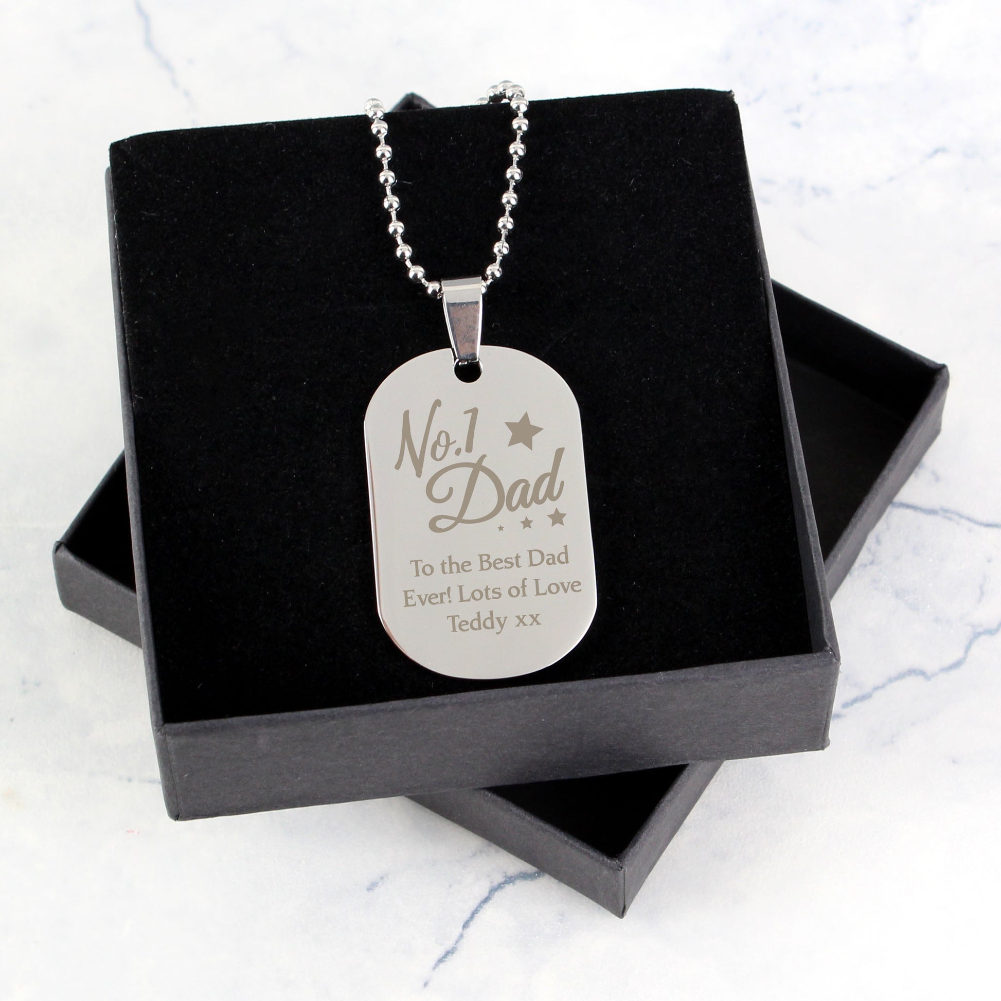 Silver dog tag necklace with engraved message in a black box on a light grey background