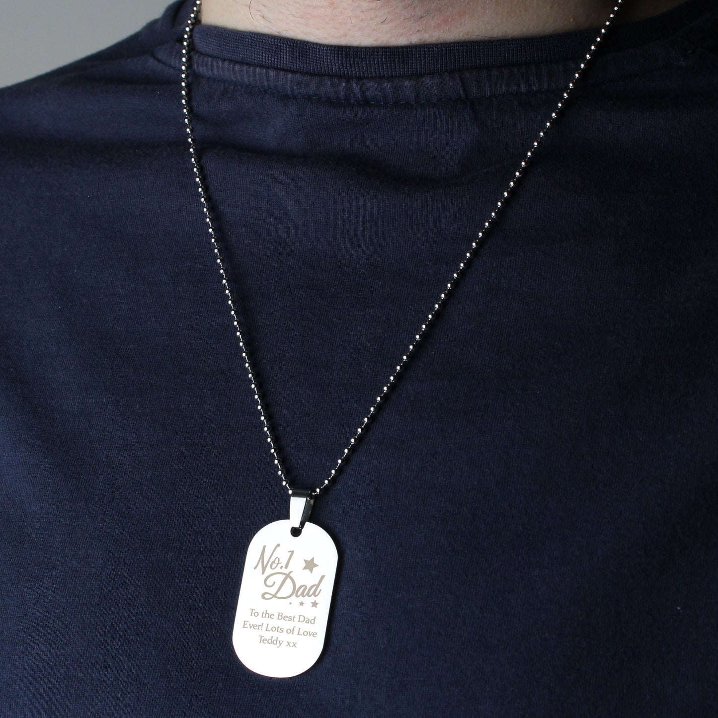 Person wearing a necklace with a 'No. 1 Dad' dog tag on a dark shirt