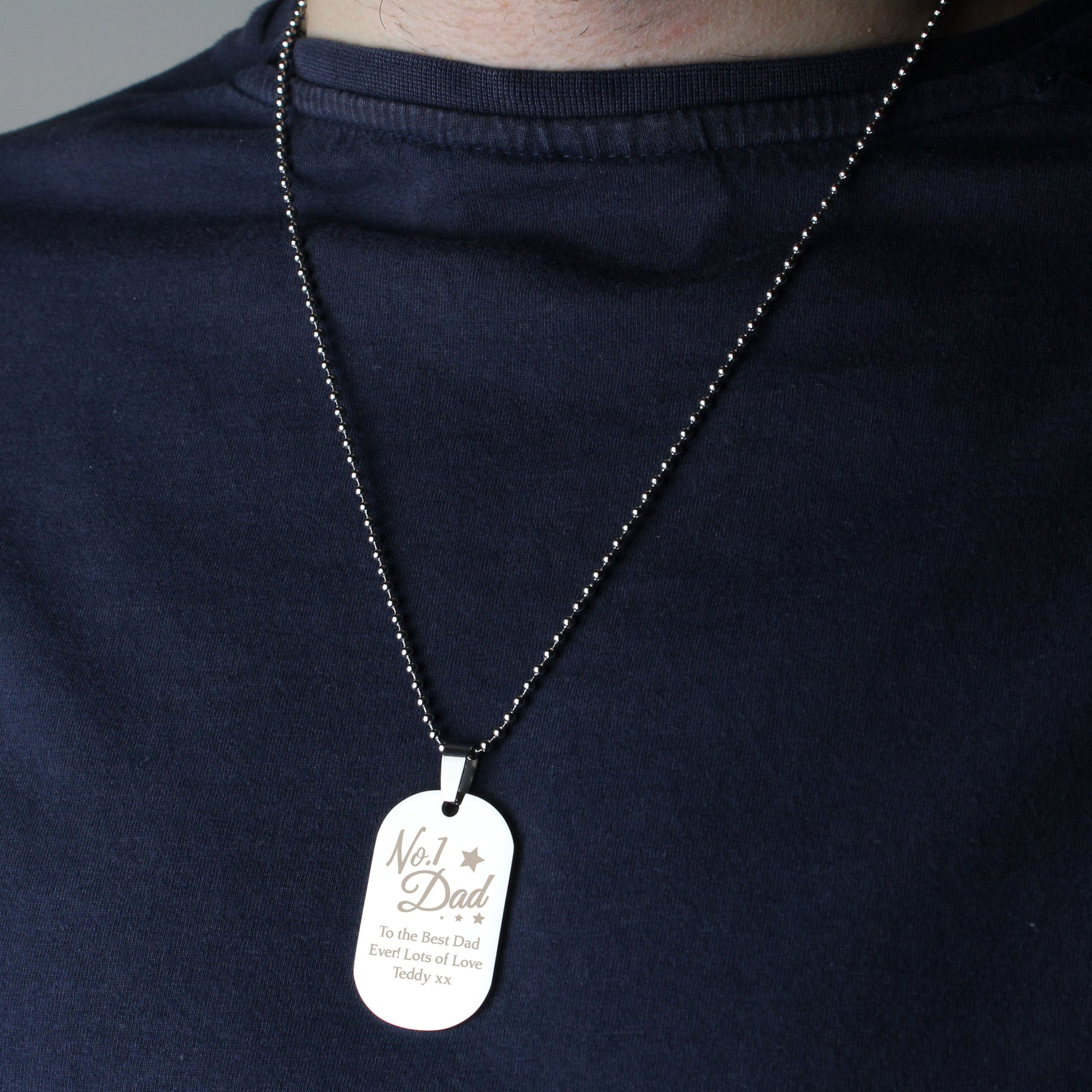 Person wearing a necklace with a 'No. 1 Dad' dog tag on a dark shirt