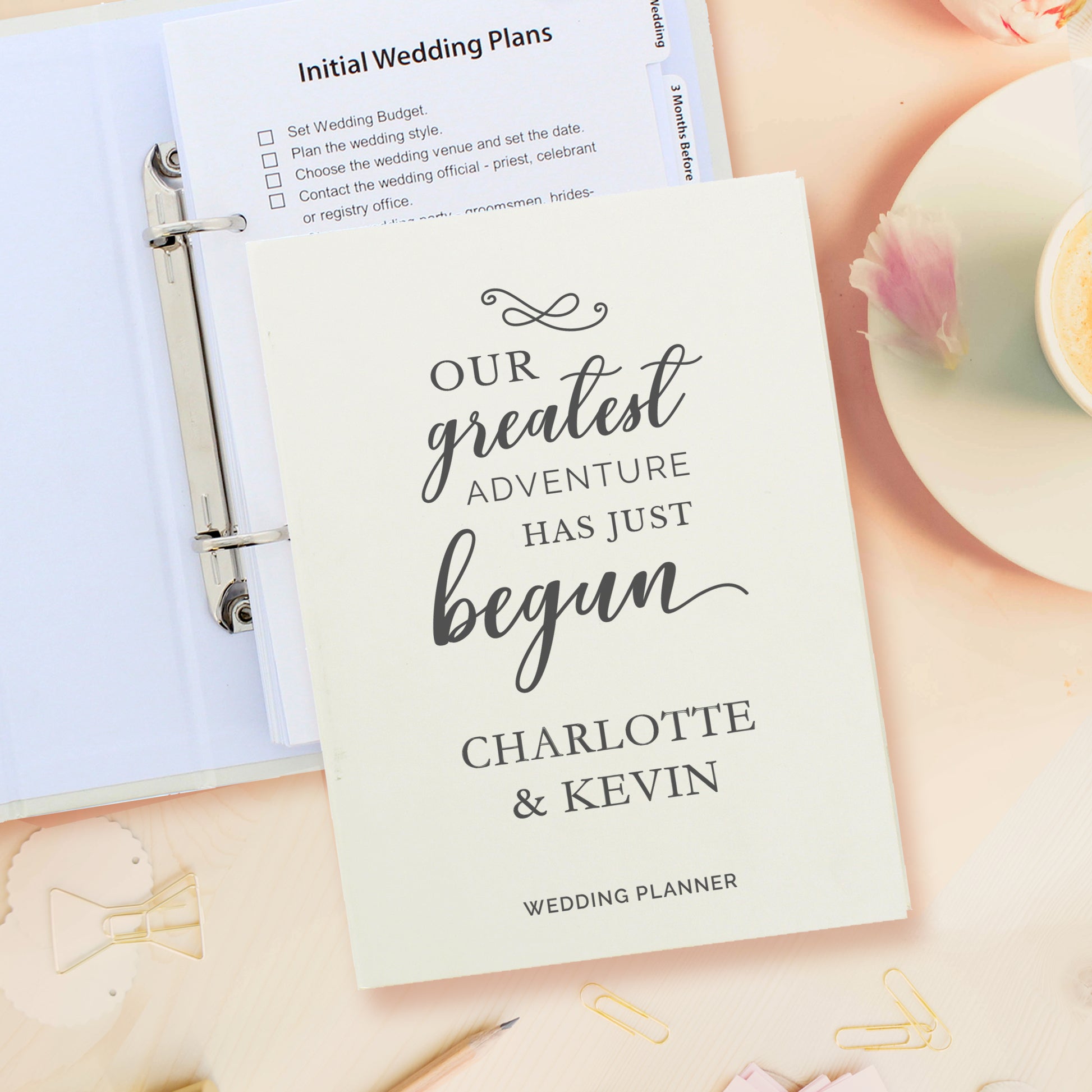 Wedding planner book with 'Our greatest adventure has just begun' text, placed on a surface with stationery items.
