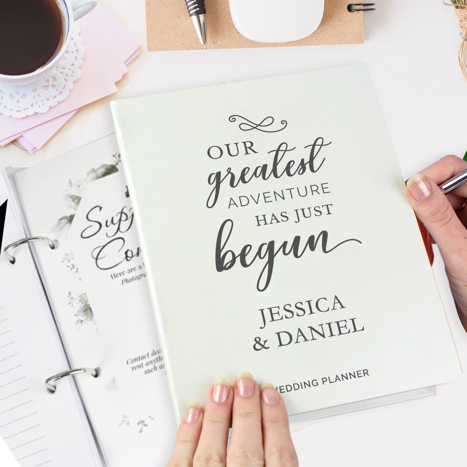 Wedding planner book with 'Our greatest adventure has just begun' text, held by a hand.