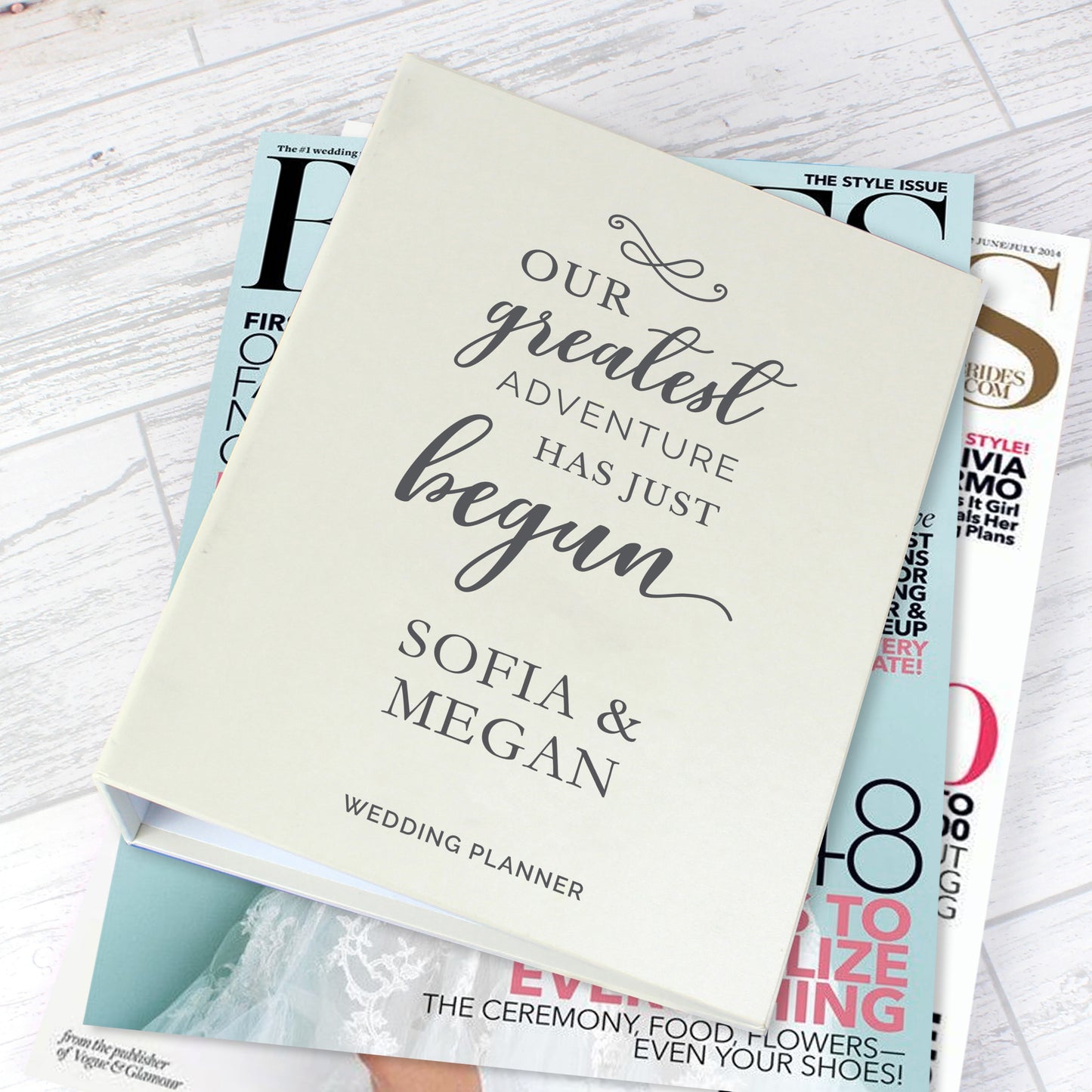 Wedding planner book with 'Our greatest adventure has just begun' text on top of magazines.