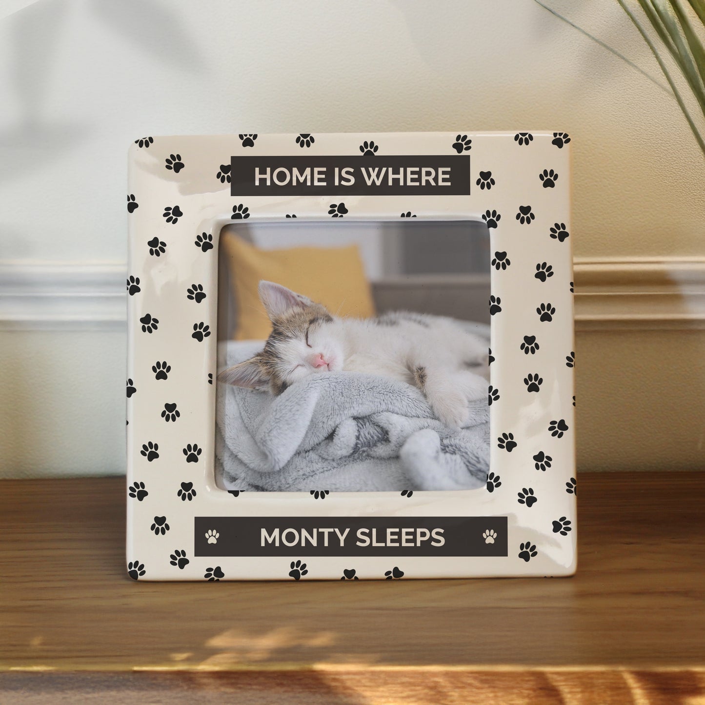 Photo frame with paw prints and text displaying a cat sleeping, on a wooden surface.