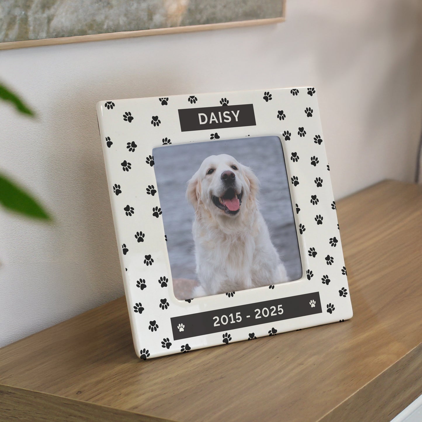 Personalised photo frame with a dog's name and years on a wooden surface.