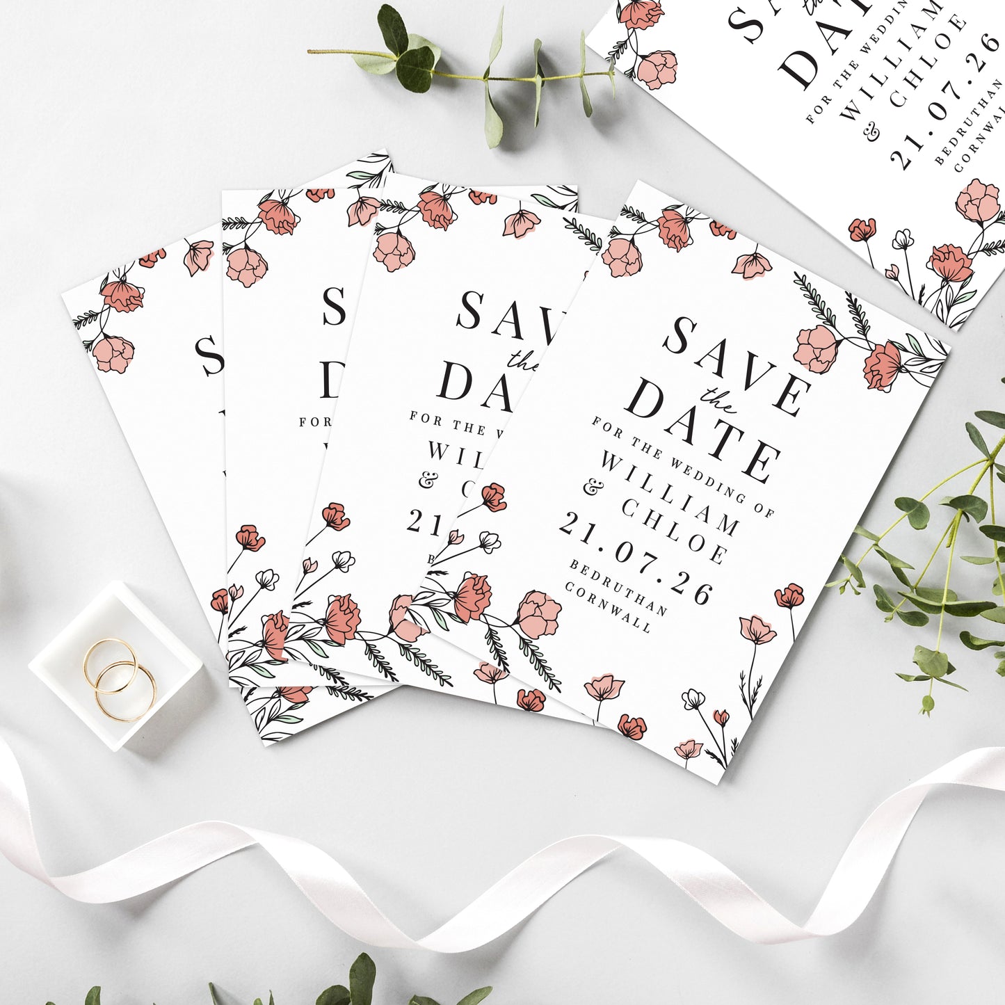 Save the date cards with floral design on a white surface with ribbons and greenery.