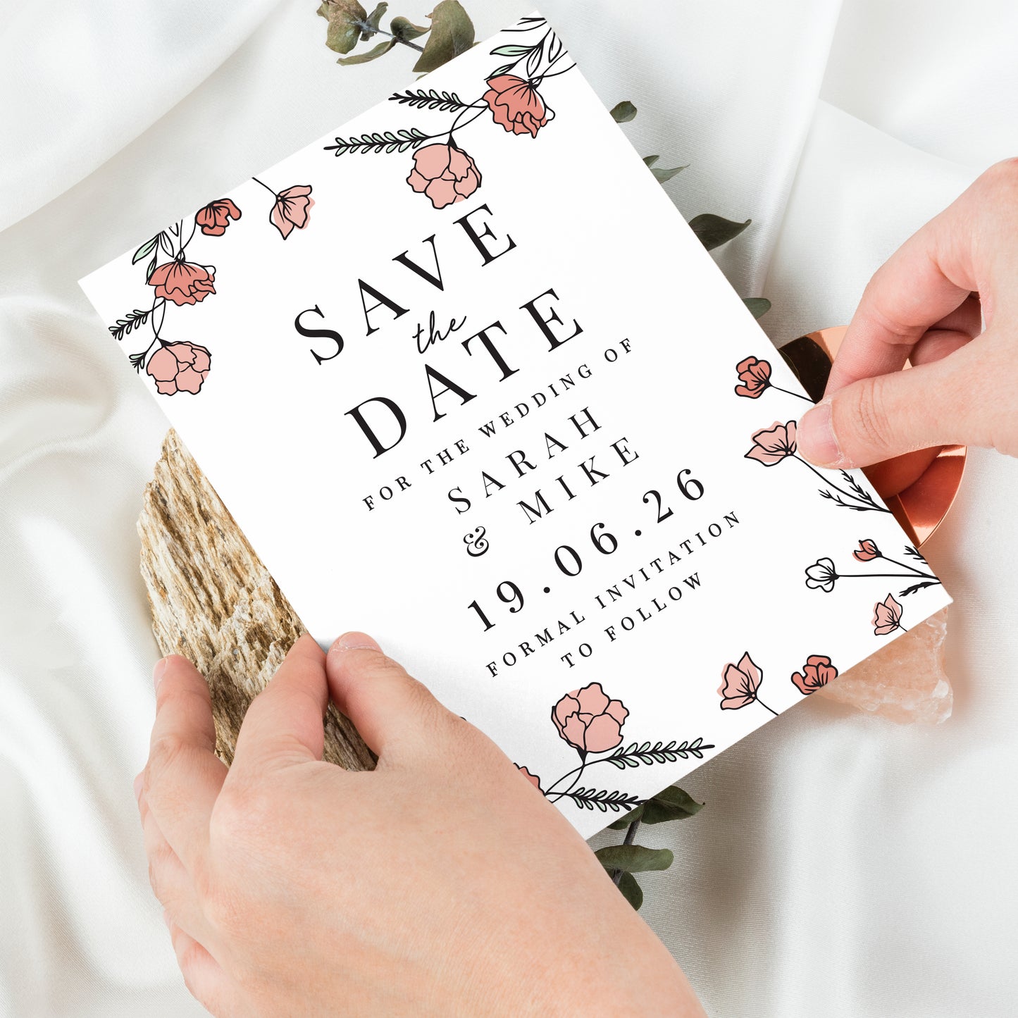 Save the date card with floral design held by hands on a light background