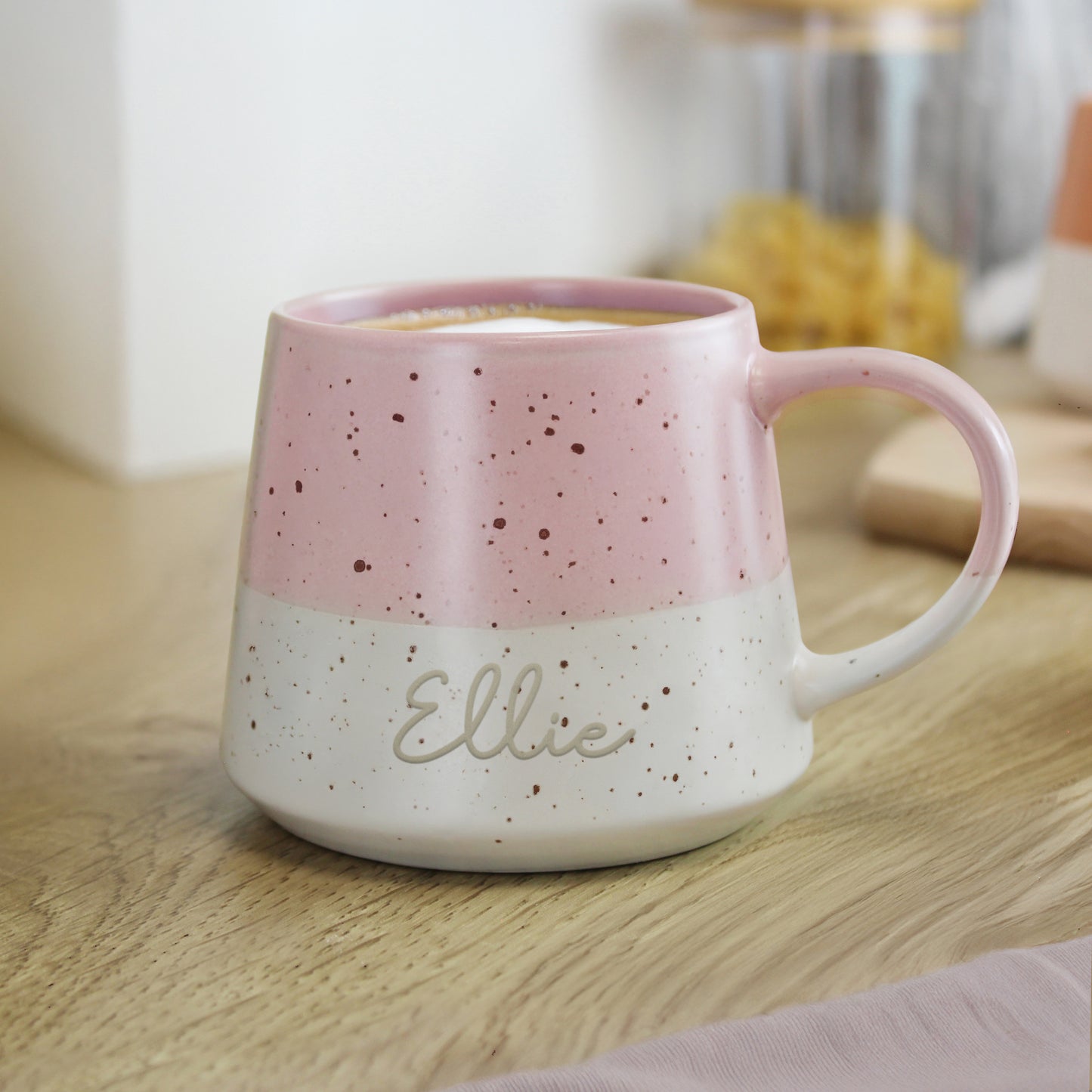 Personalised pink and white speckled mug with 'Ellie' on a wooden surface