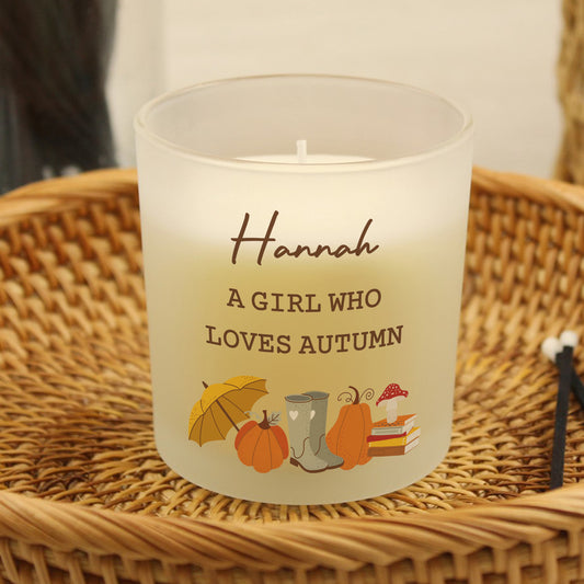 Personalised candle with 'Hannah A Girl Who Loves Autumn' text and autumn-themed illustrations on a woven surface.