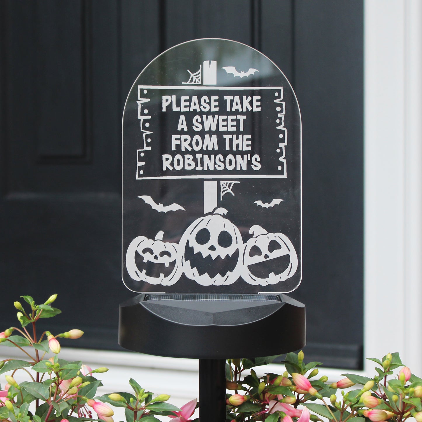 Personalised Pumpkin images solar light standing in  flower bed. Text reads Please take a sweet from the Robinson's.