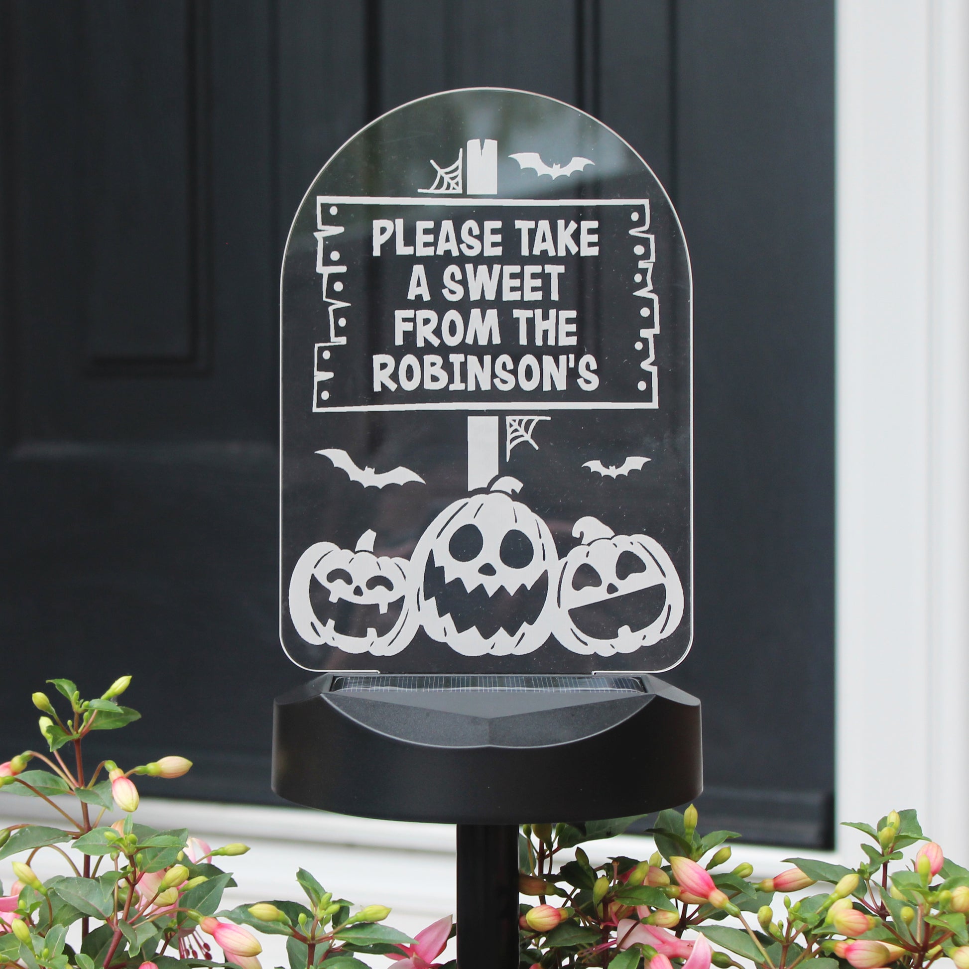 Personalised Pumpkin images solar light standing in  flower bed. Text reads Please take a sweet from the Robinson's.