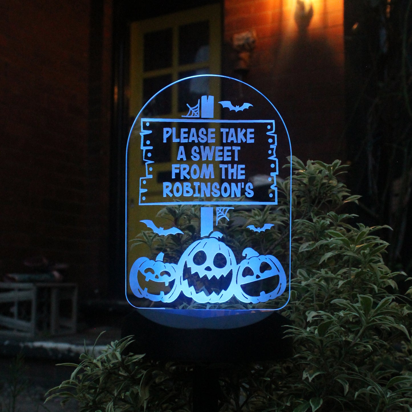 Halloween-themed decorative sign with pumpkins and text 'Please take a sweet from the Robinson's' in a dark outdoor setting.
