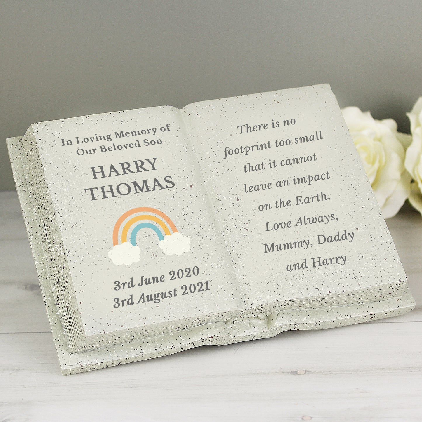 Memorial book with engraved text and rainbow design on a white surface.