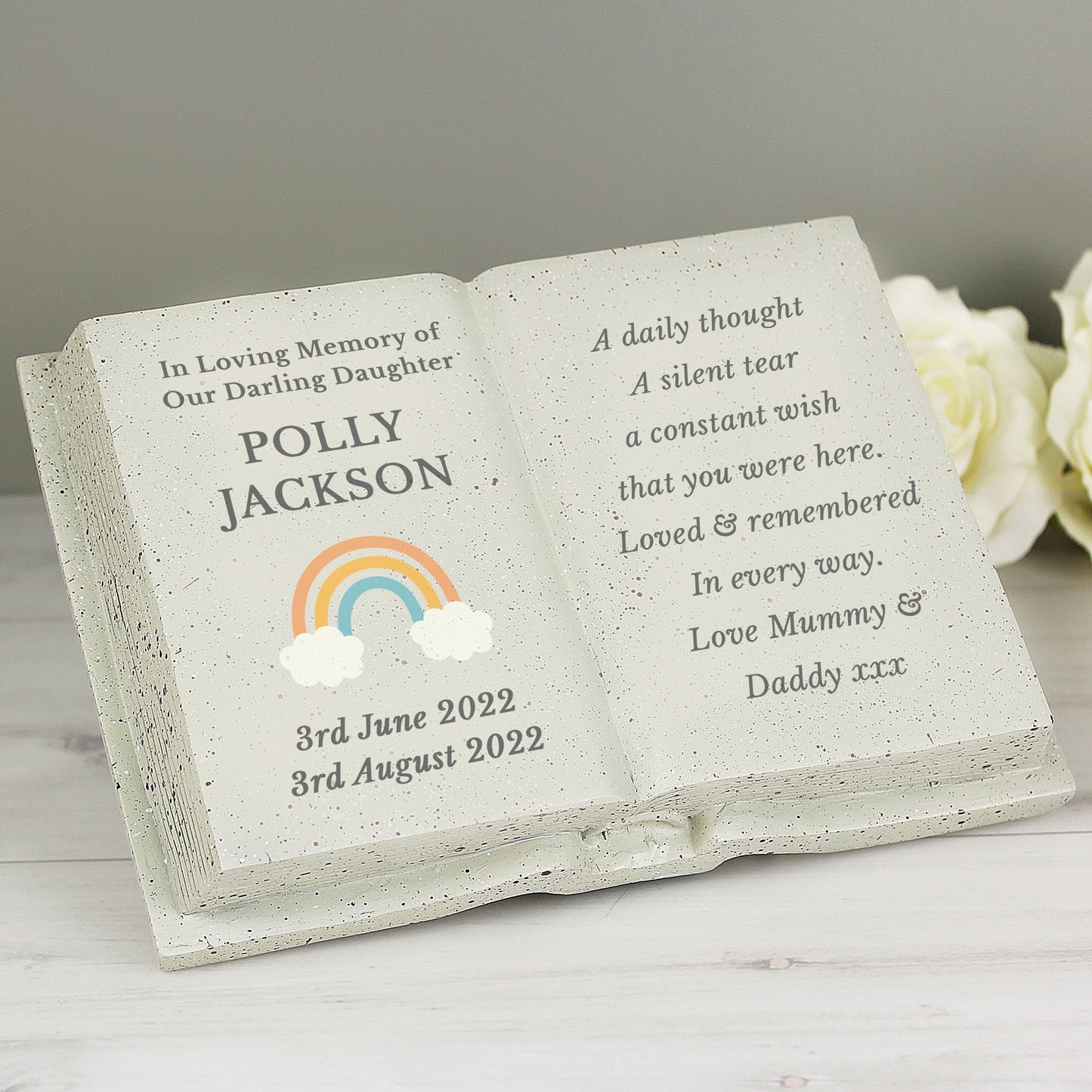 Memorial stone book with engraved text and rainbow design on a white surface.
