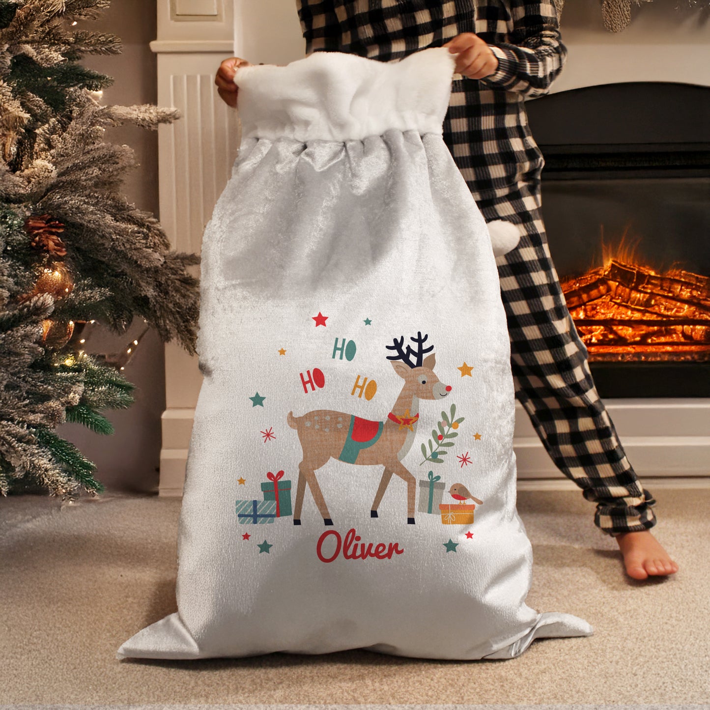 Person holding a Christmas-themed sack with a reindeer design and 'Ho Ho Ho Oliver' text, in front of a fireplace.