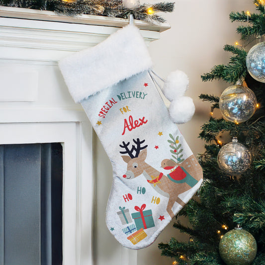 White polyester Christmas stocking with reindeer image and the name Alex hanging on a shelf by the Christmas tree.
