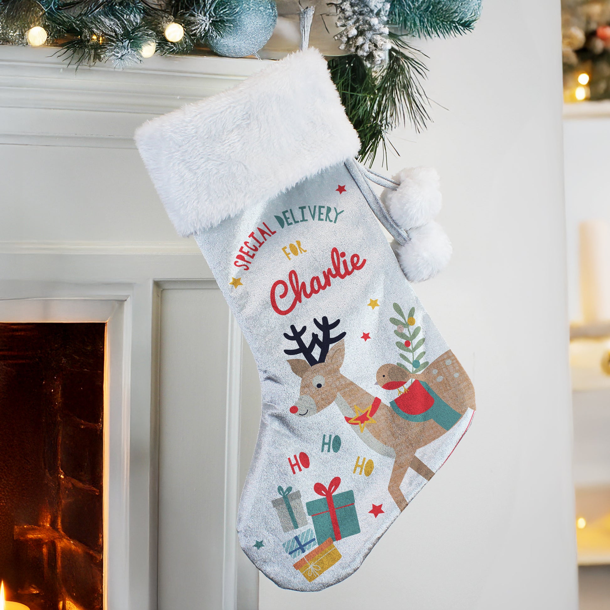Personalised Christmas stocking with reindeer design hanging by a fireplace.