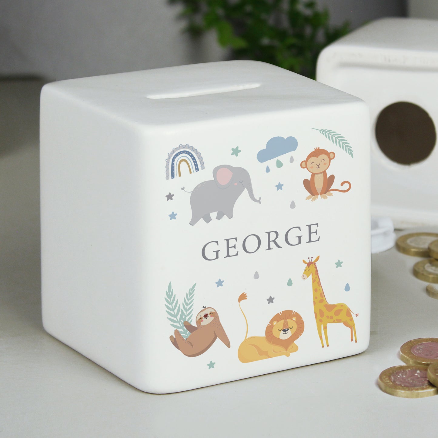 White ceramic square money box with the name 'GEORGE' with safari animal and rainbow images  shown on a white shelf alongside coins.