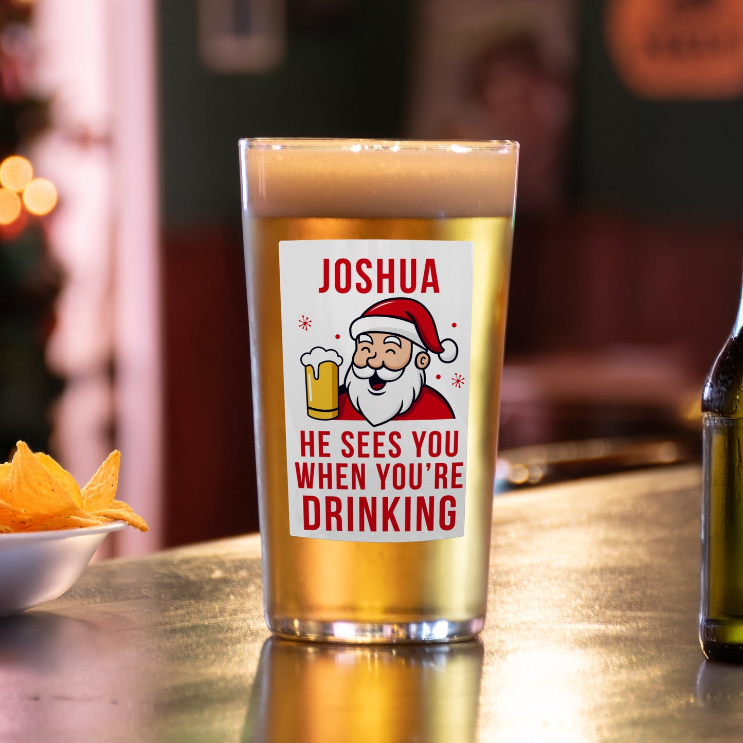 Beer glass with a Santa Claus label on a bar counter with snacks and a bottle.