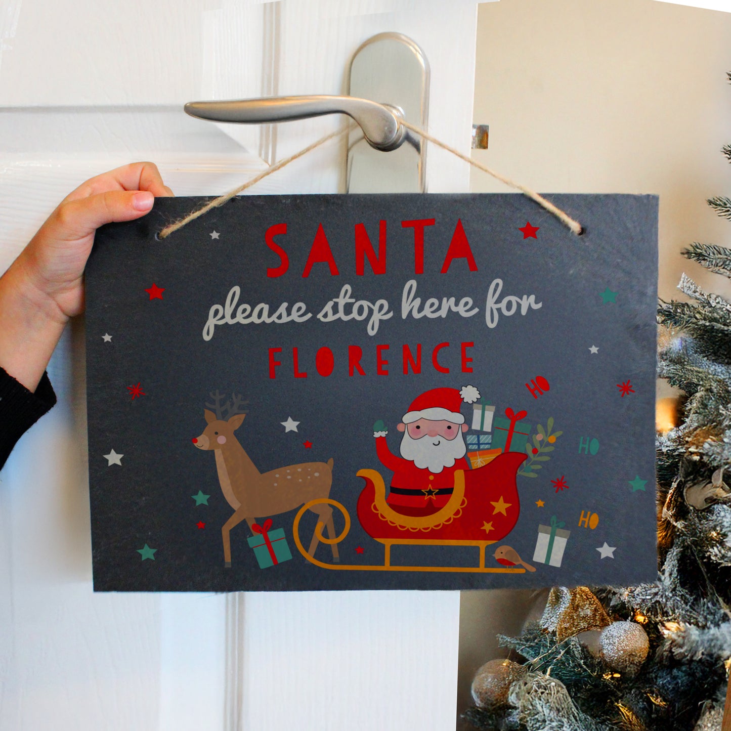 Sign hanging on door next to Christmas tree. Red sleigh with Santa and reindeer. Personalised with Santa please stop here for Florence.