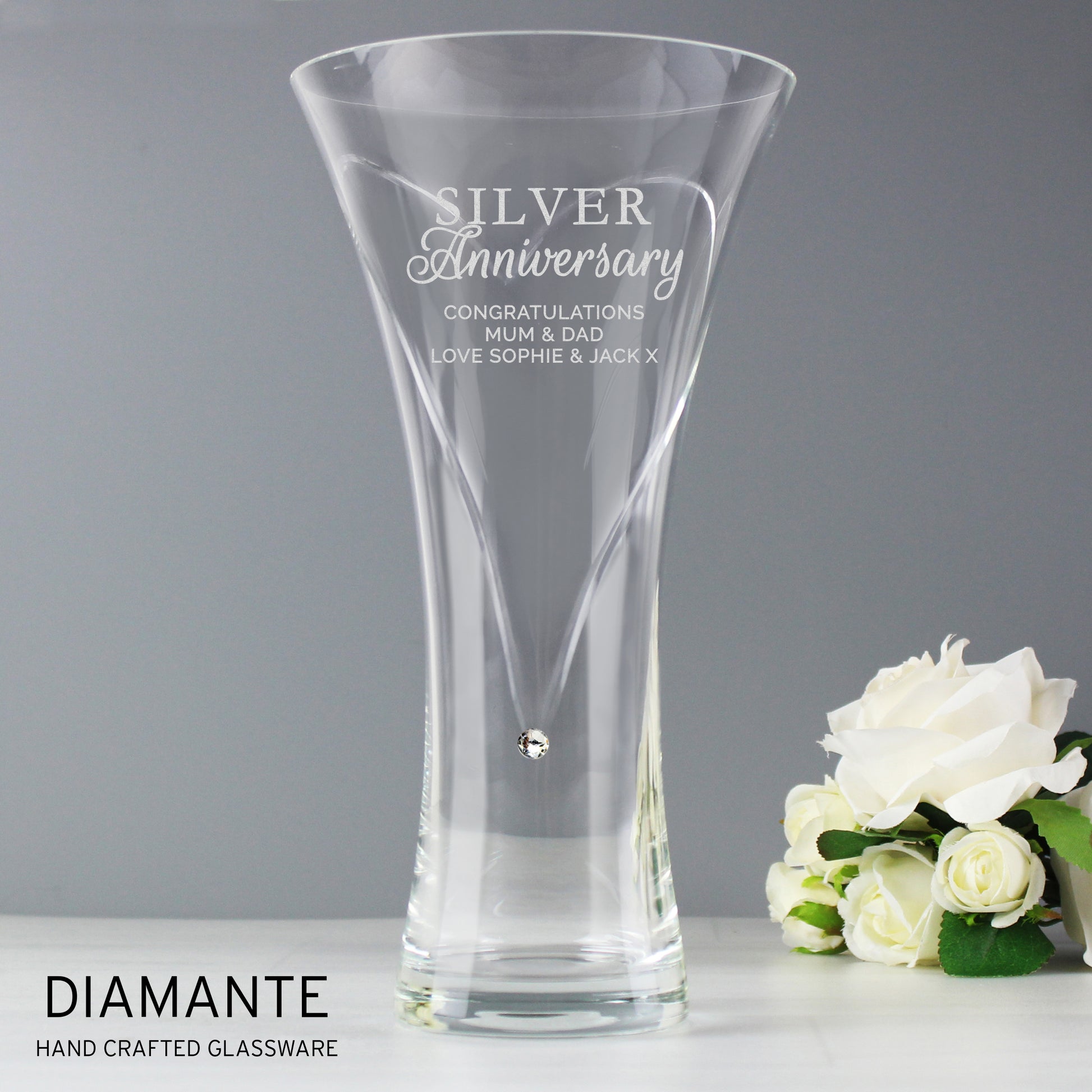 Clear glass vase with engraved text and white roses on a gray background