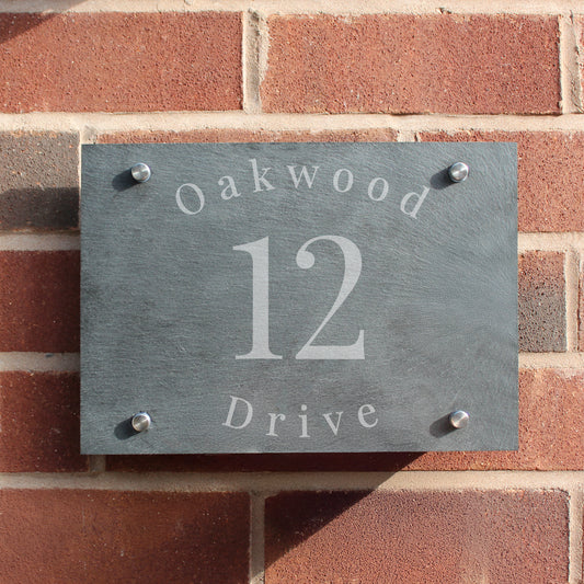 Slate house number sign with 'Oakwood 12 Drive' on a brick wall