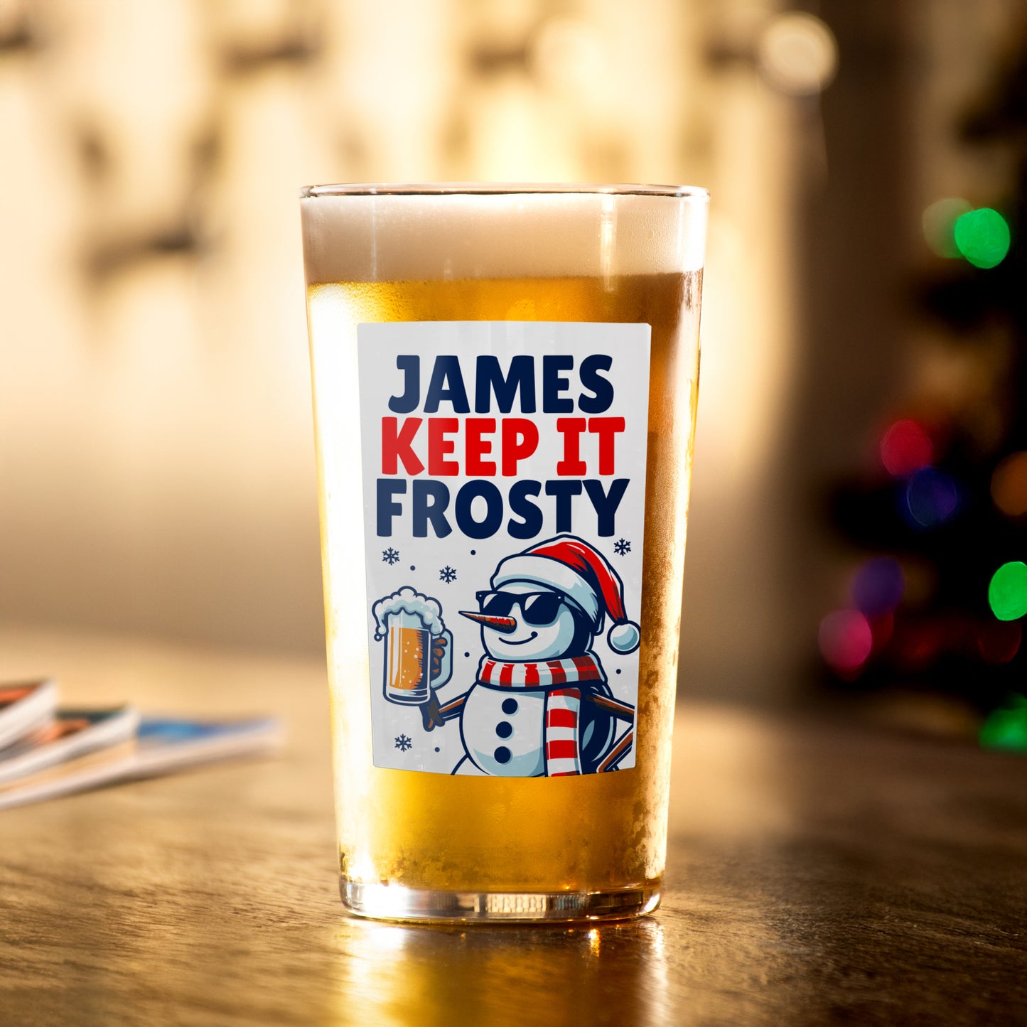 Glass with a snowman design and text on a wooden surface with blurred lights in the background.