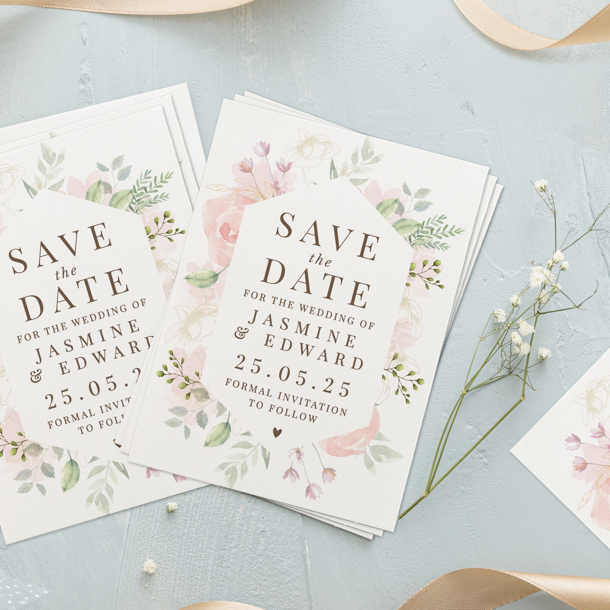 Floral 'Save the Date' cards for a wedding on a light blue surface with small white flowers.