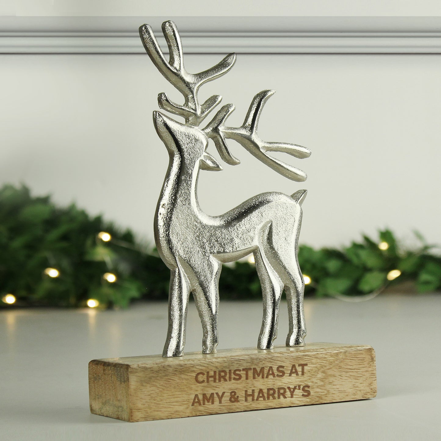 Silver reindeer figurine on a wooden base with 'Christmas at Amy & Harry's' engraving, against a festive background.