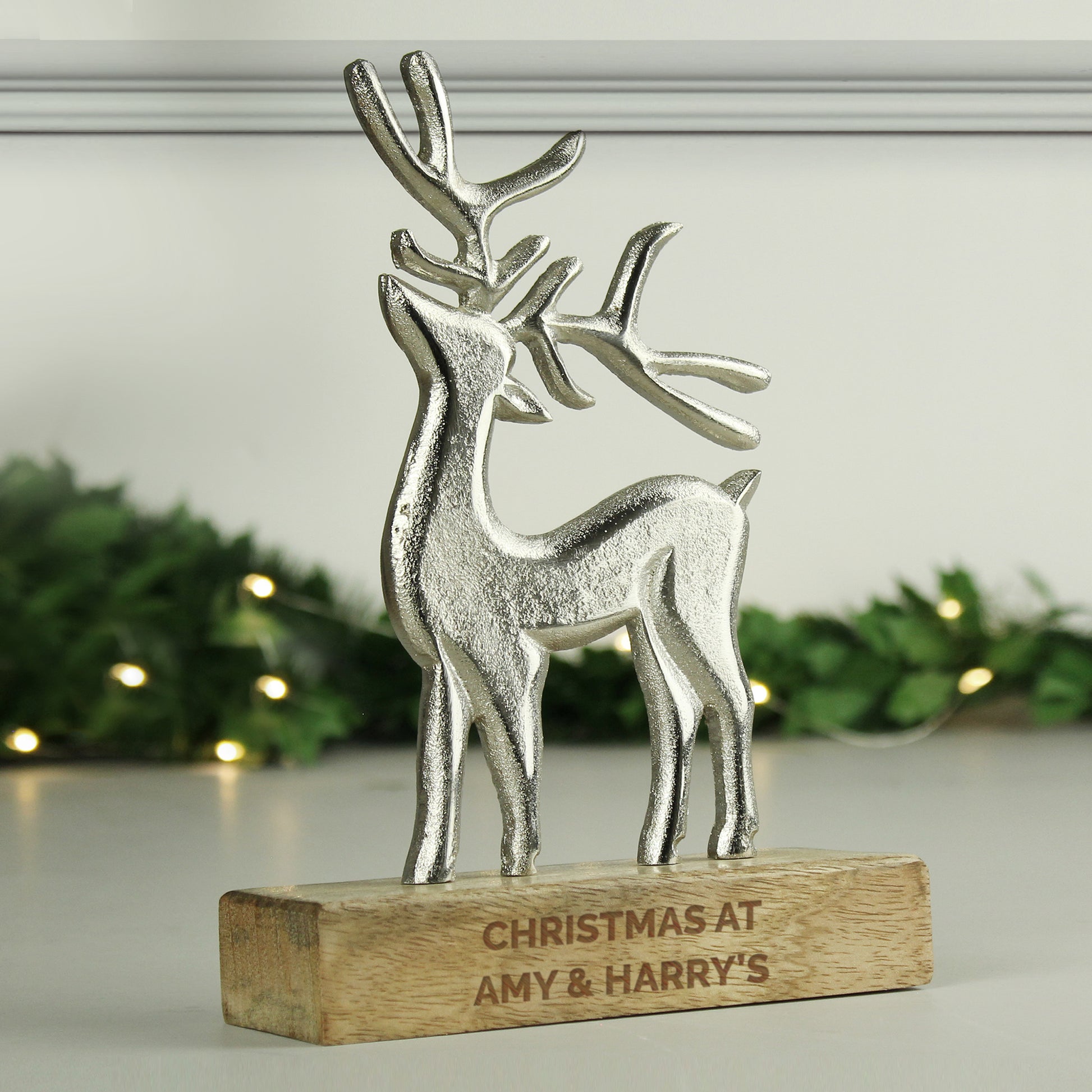 Silver reindeer figurine on a wooden base with 'Christmas at Amy & Harry's' engraving, against a festive background.