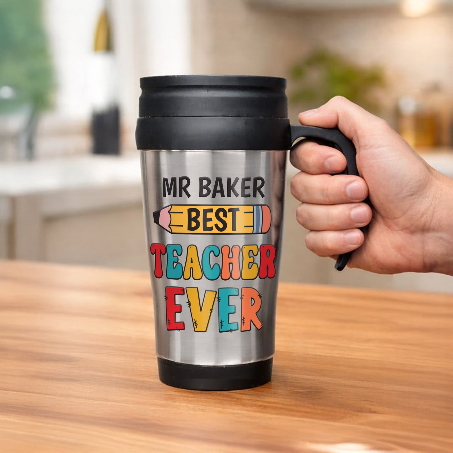 Person holding a travel mug with 'MR BAKER BEST TEACHER EVER' text in a kitchen setting