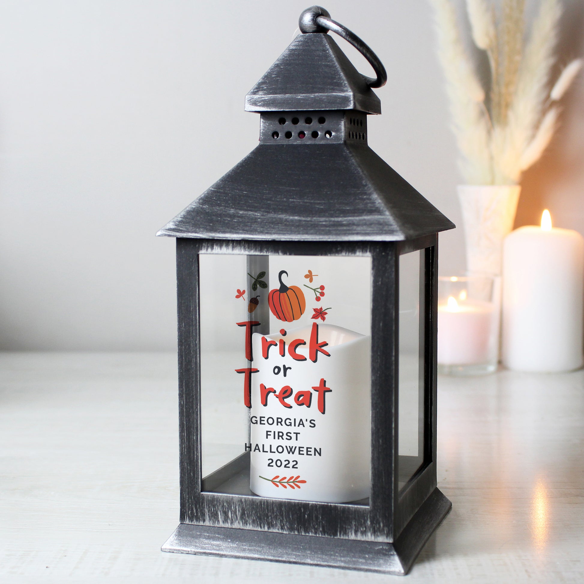 Black lantern with a candle featuring 'Trick or Treat' text and pumpkins, set against a neutral background.