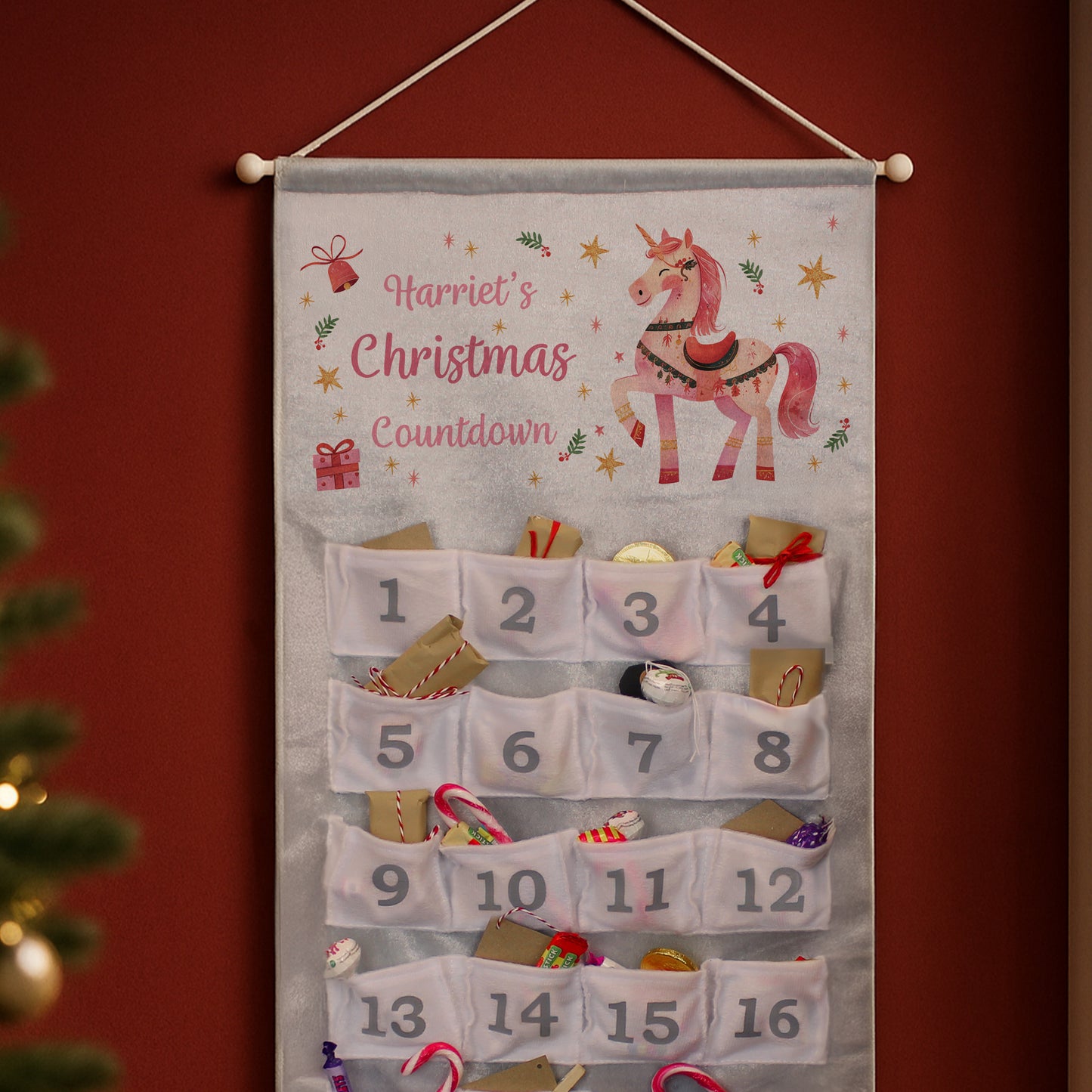Personalised Christmas countdown calendar with a unicorn design on a red wall.
