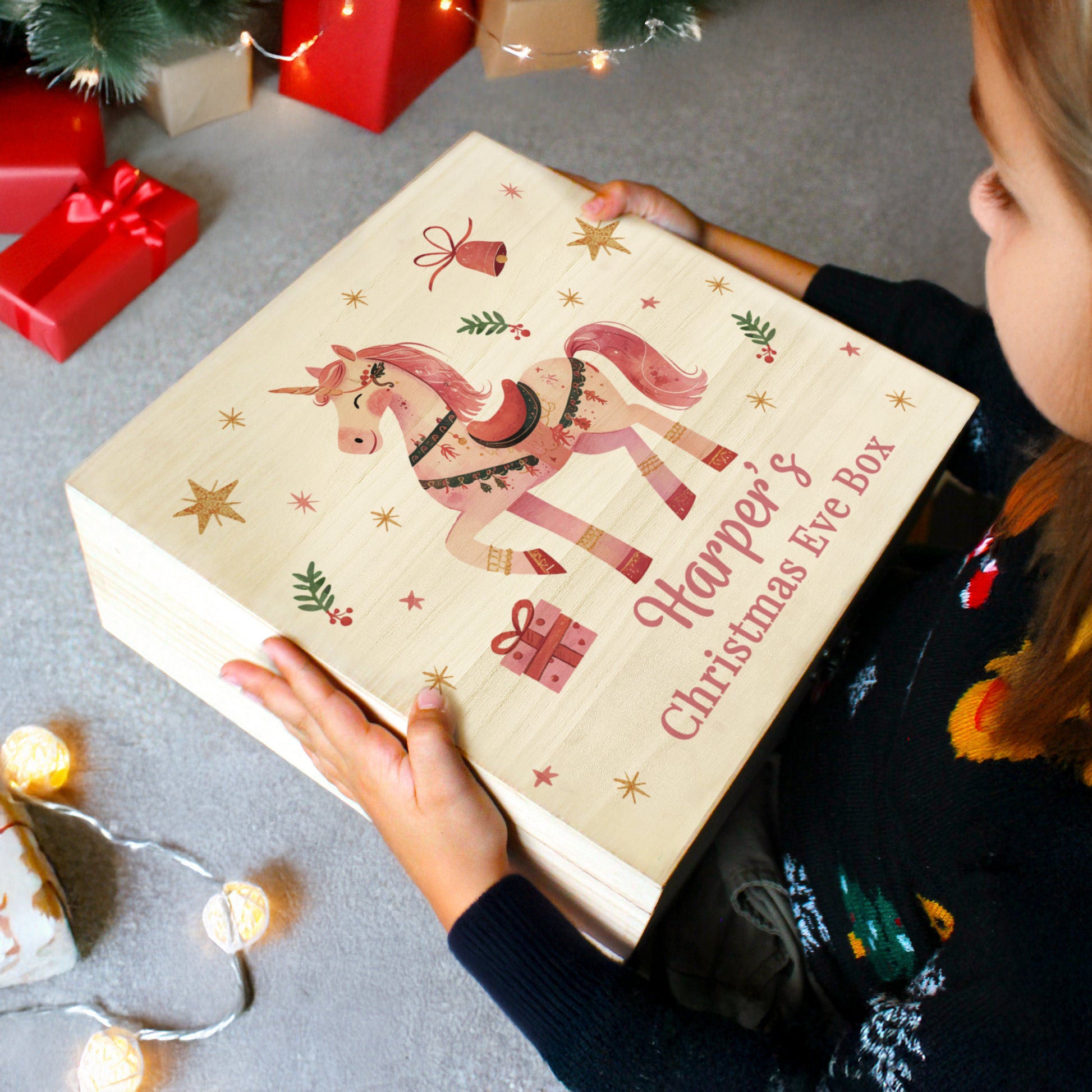Child holding Christmas Eve wooden box with unicorn image. Text reads Harper's Christmas Eve Box.