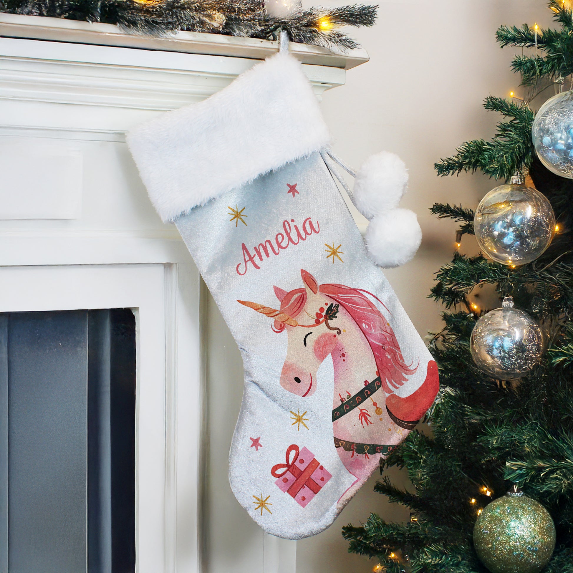 Personalised unicorn Christmas stocking hanging by a fireplace with a decorated tree in the background.