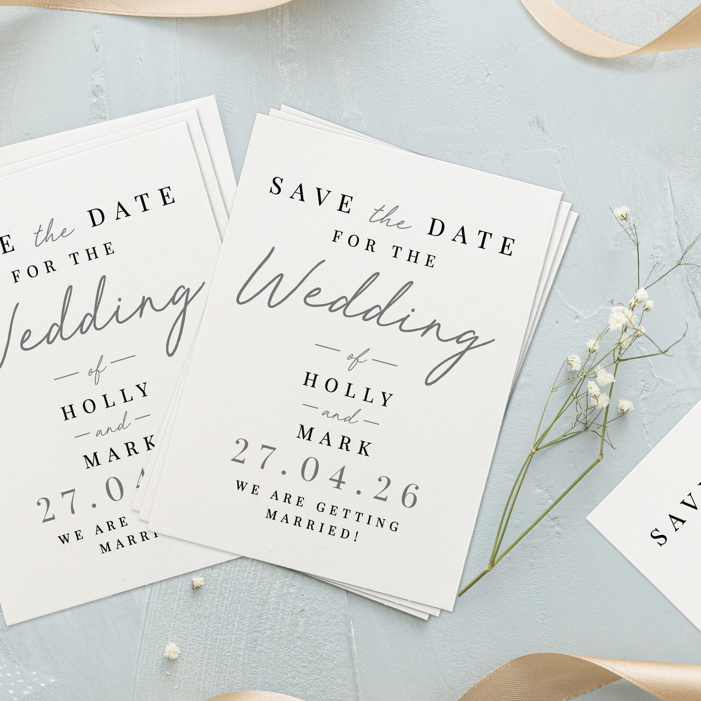 Wedding save the date cards on a light blue surface with small white flowers.