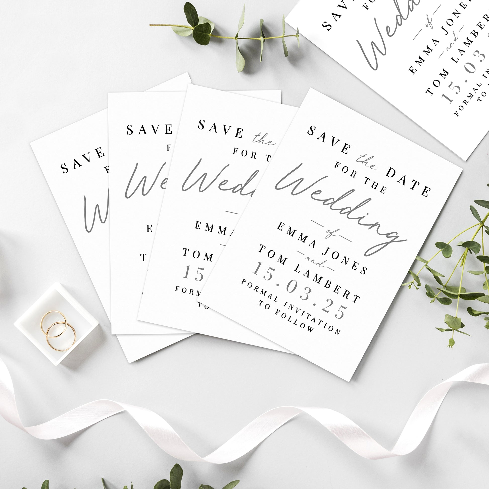Save the date cards for a wedding on a white surface with greenery.