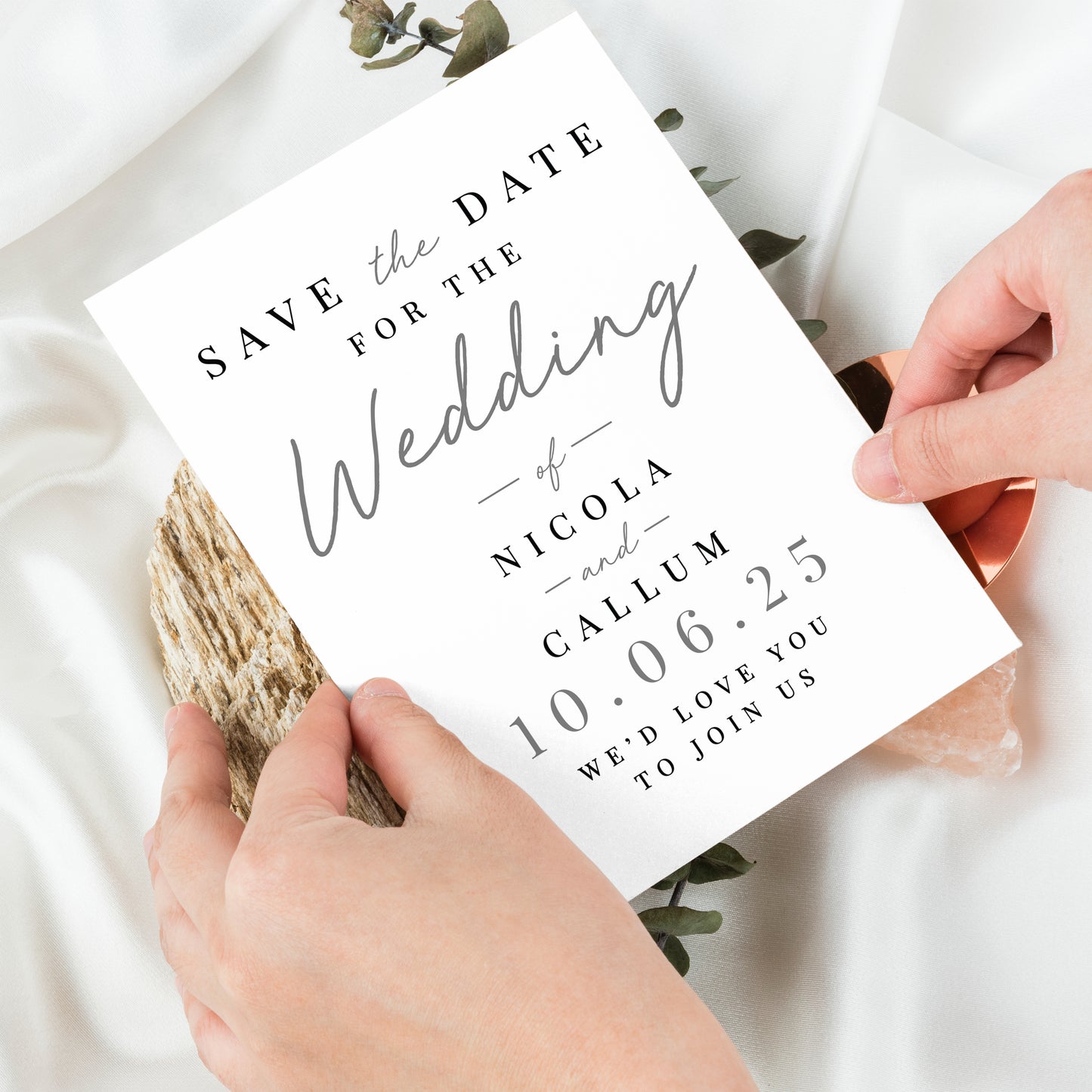 Hands holding a 'Save the Date' wedding card with text and a wooden stick.